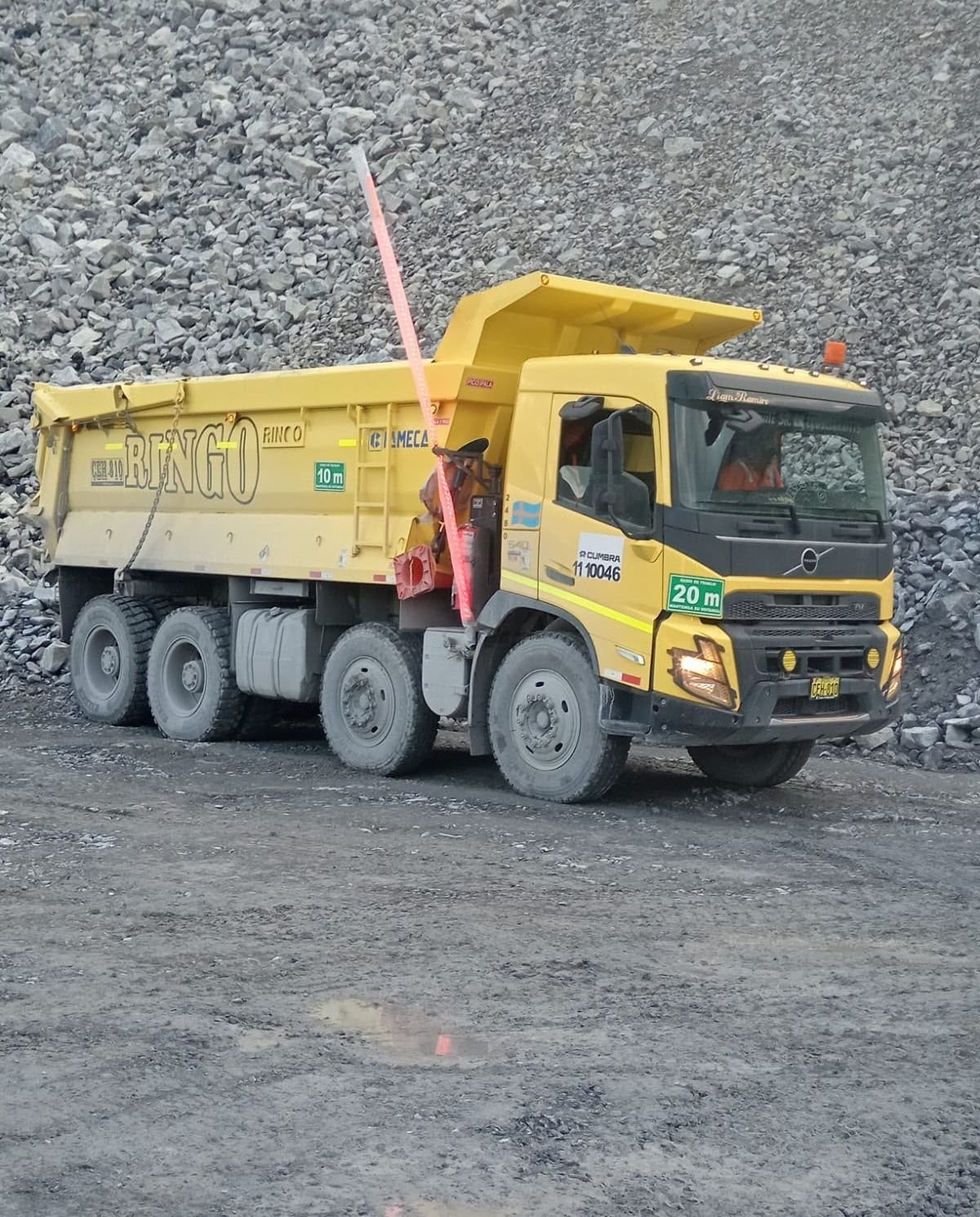 Operator driving a Ringo dump truck in front of a rock slope at a mining operation.